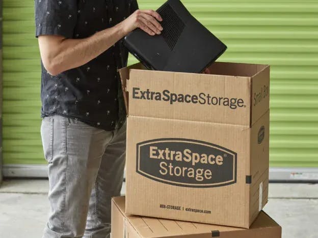 Man packing an Extra Space Storage moving box in front of green storage unit door. 
