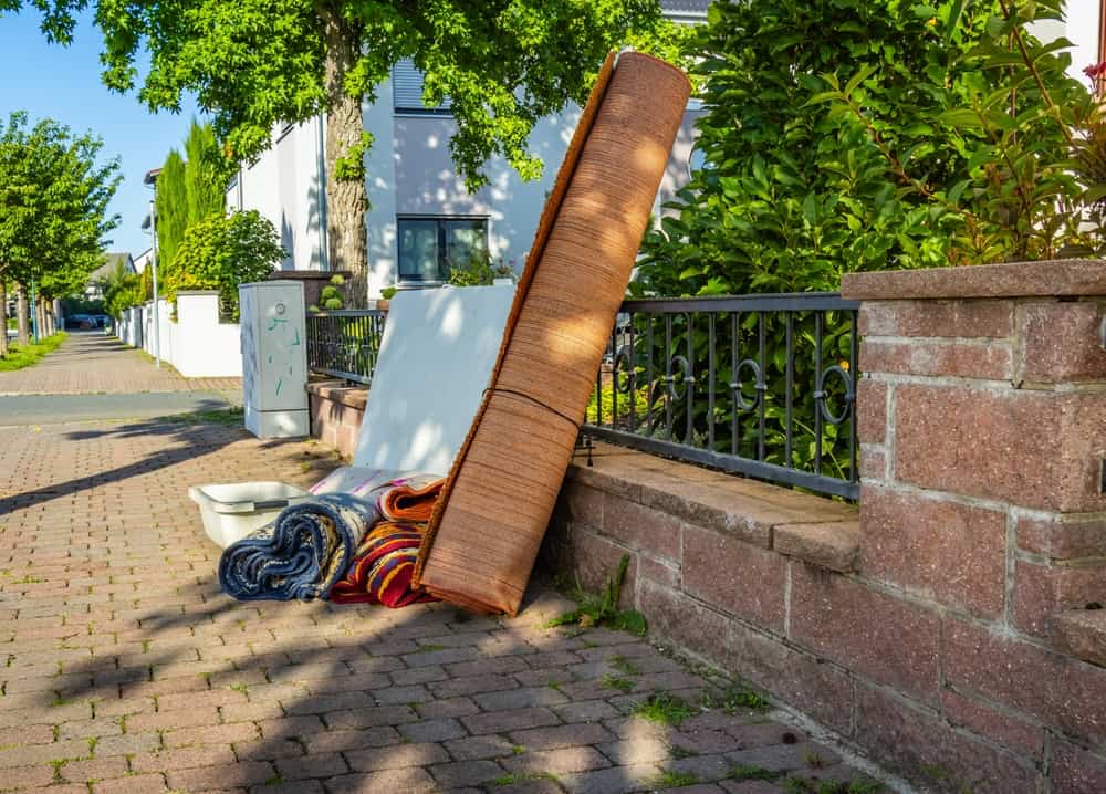 Junk like rolled up rug, mattress, laundry basket, and other items on side of road waiting for junk removal company.