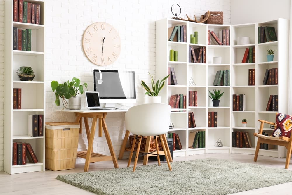 A desk, chair, bookshelf, and computers in a bright home office.