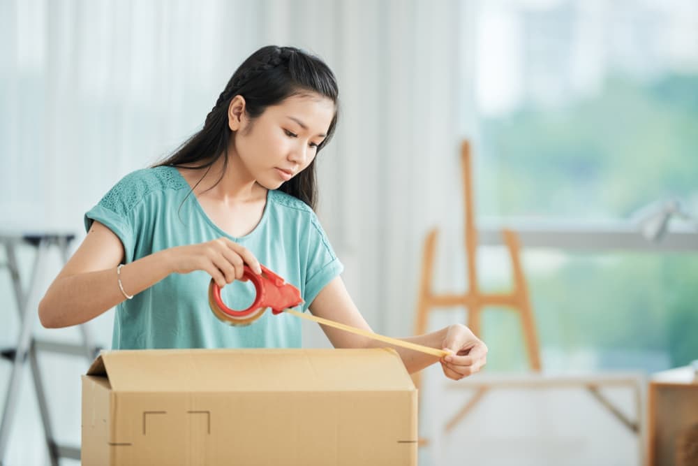 A woman closing a moving box with tape
