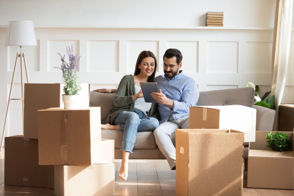 A couple reading from a tablet surrounded by moving boxes