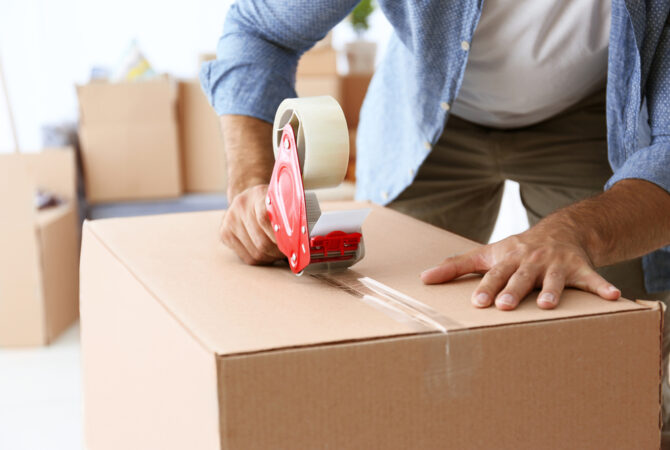 Man sealing moving box with packing tape