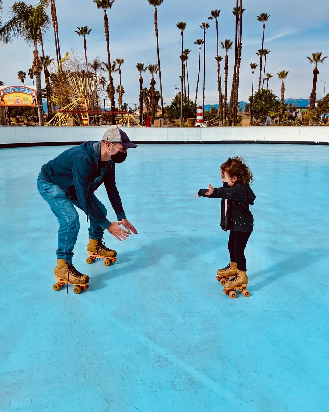 Man wearing roller skates squatting to catch his young child, who is skating toward him. Photo via Instagram user @fiesta_village