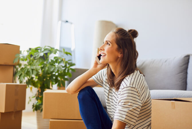 Young woman talking on phone with moving boxes around her