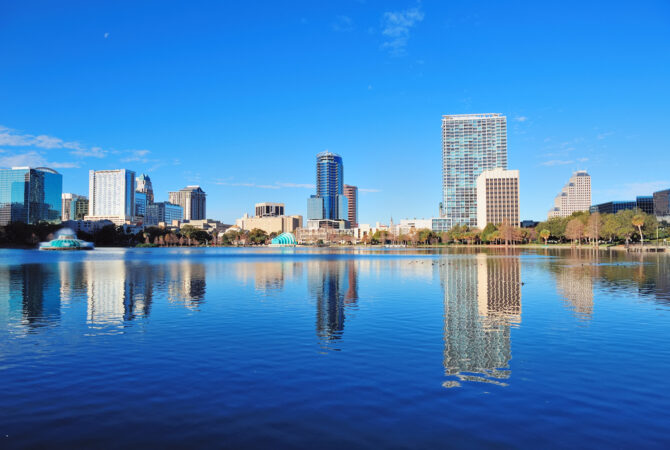 Skyline of tall buildings by water on sunny day in Downtown Orlando.