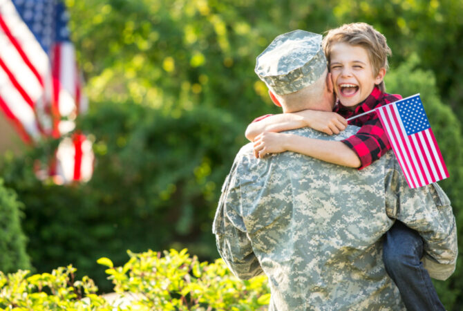 Member of the Armed Forces Hugging a Child Holding an American Flag