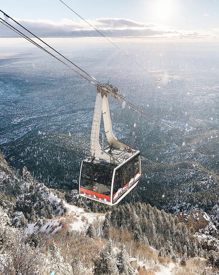 The Sandia Tram in Santa Fe New Mexico on a calm winter day with snow falling around the tram and a beautiful view of the landscape below. Photo by instagram user @bledileno