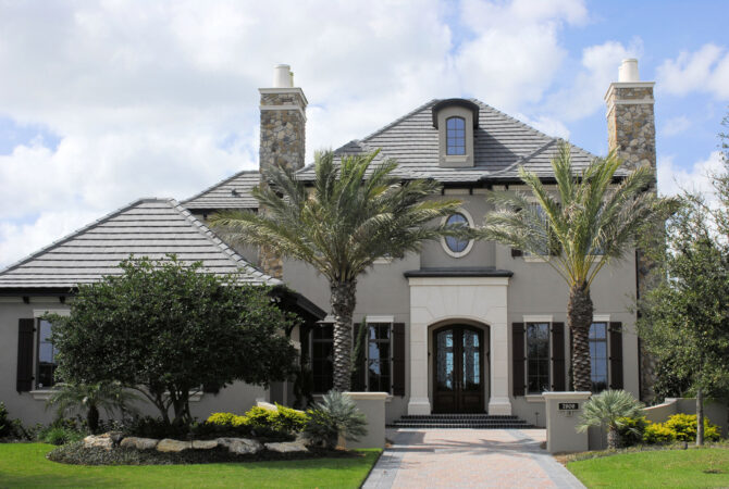 A grey house with colums, and green tropical trees out front.