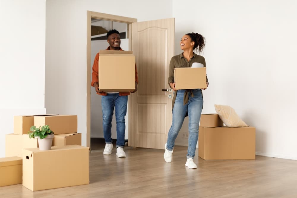 Young couple moving into a home carrying moving boxes.