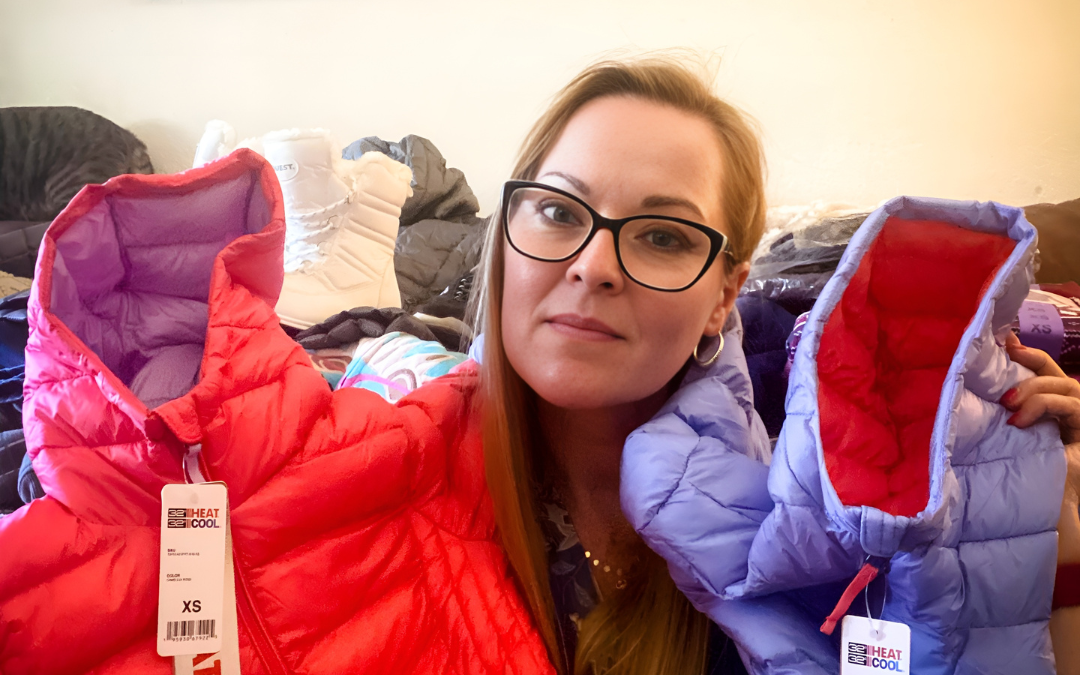 Anastasia Krecklow holding two children's winter coats on either side of her face during the Winter Survival Essentials Drive for Ukraine put on by the Central Park Angels