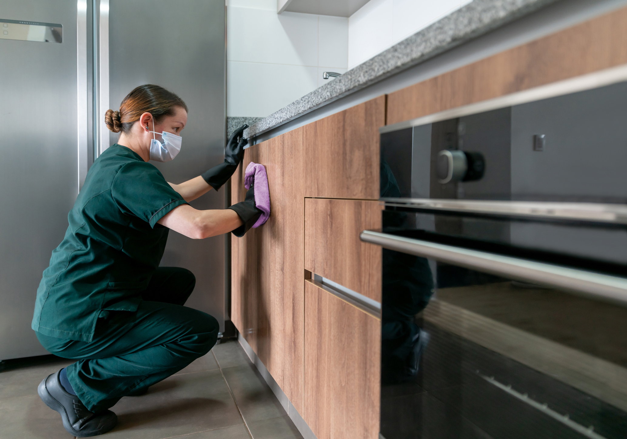 moving into a new house - Latin American cleaner wearing a facemask while cleaning the kitchen at a house